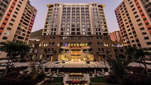 A multi-story hotel with a central entrance, surrounded by greenery and a decorative pool area. - Nujiang East Wenhao hotel (Lushui)