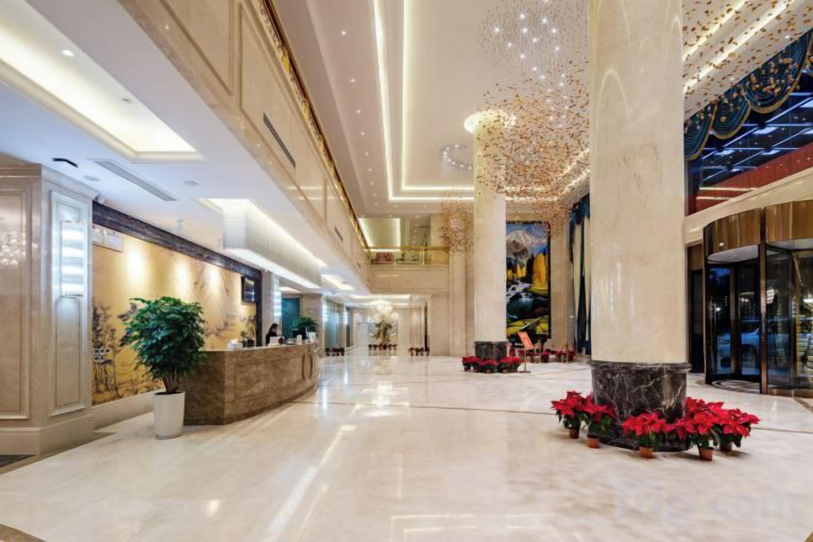 Een ruime lobby met een receptiebalie, brede kolommen en een hoog plafond met decoratieve verlichting.