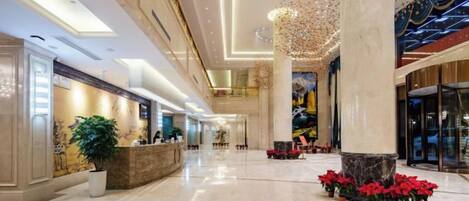 Un lobby espacioso con mostrador de recepción, grandes columnas y un techo alto con iluminación decorativa.
