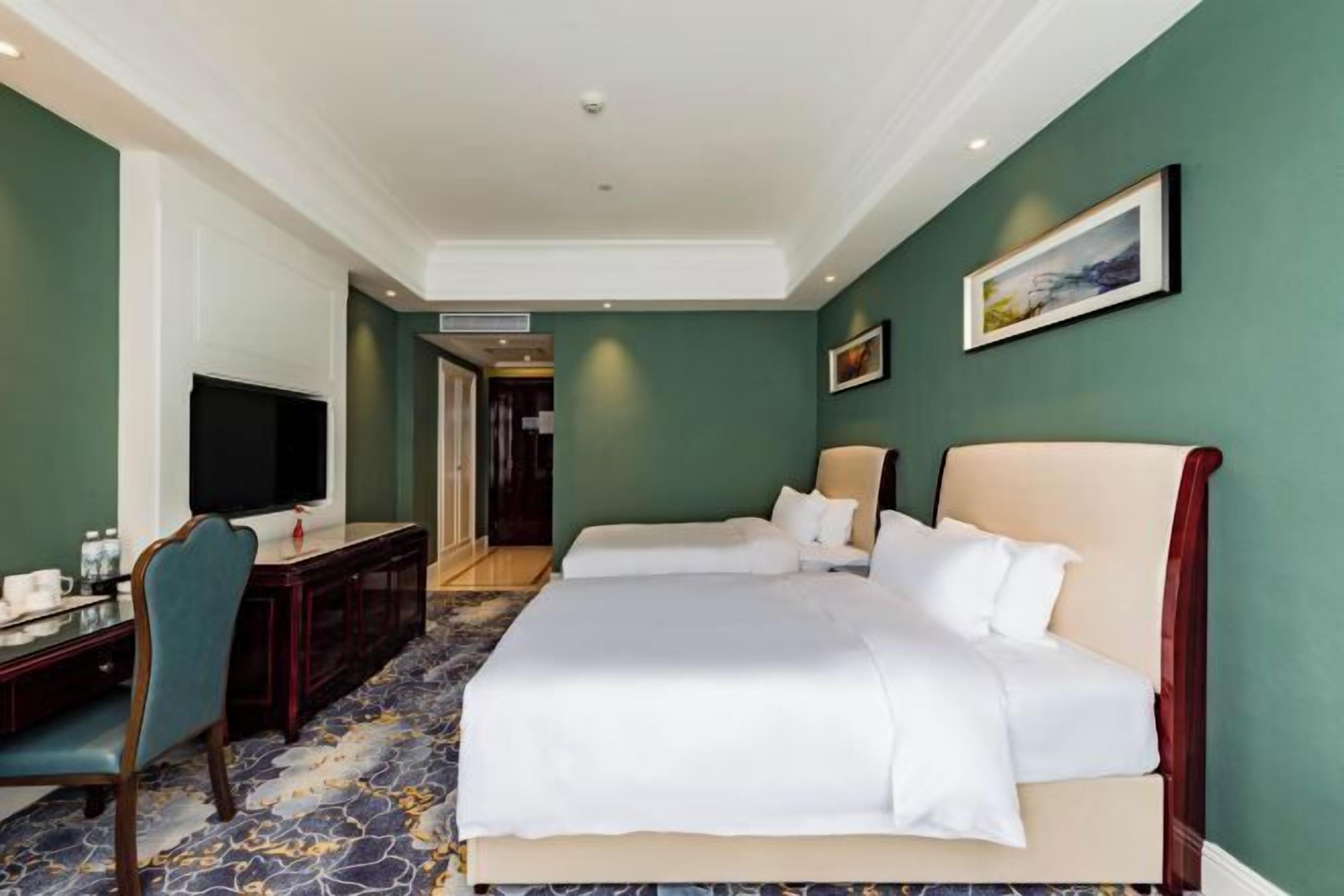 A hotel room with a large bed, a desk with a chair, a television, and a framed picture on the wall.
