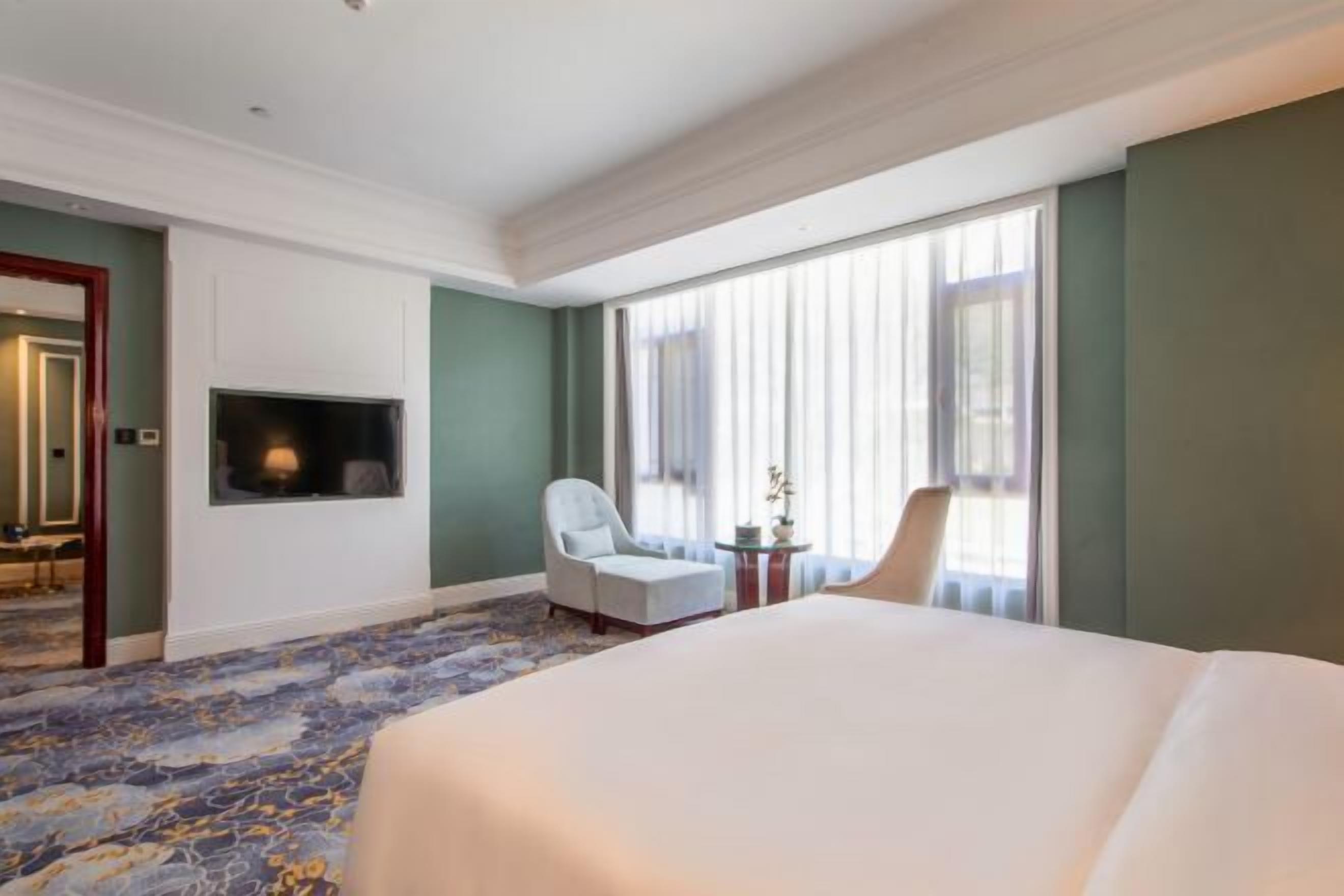 Une chambre d’hôtel avec un grand lit, un téléviseur fixé au mur, une chaise et une petite table agrémentée d’une plante.