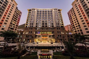 A multi-story hotel with a central entrance, surrounded by well-maintained gardens and palm trees. - Nujiang East Wenhao hotel (Lushui)
