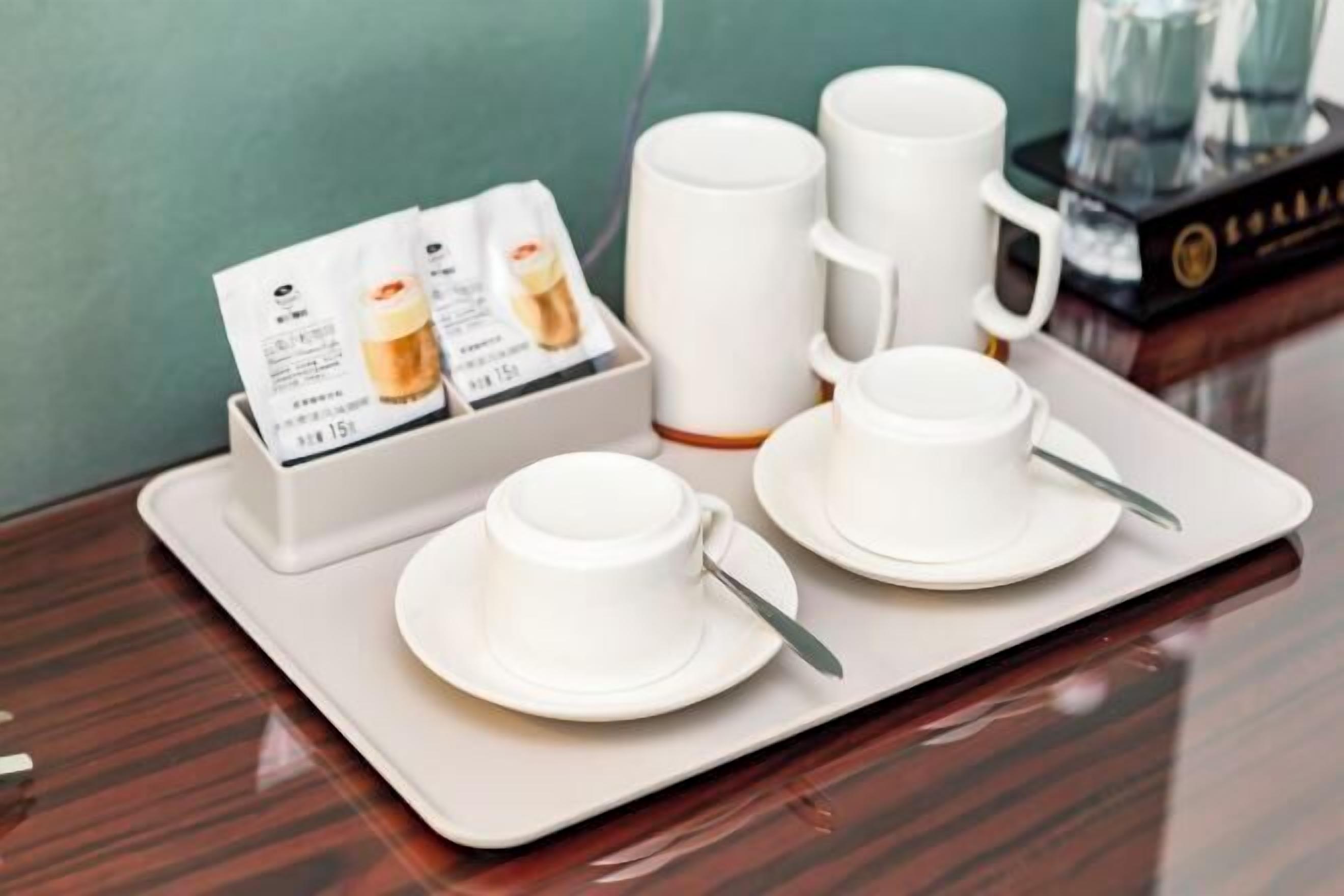 A tray with white cups and saucers, a menu, and a water bottle on a wooden table.