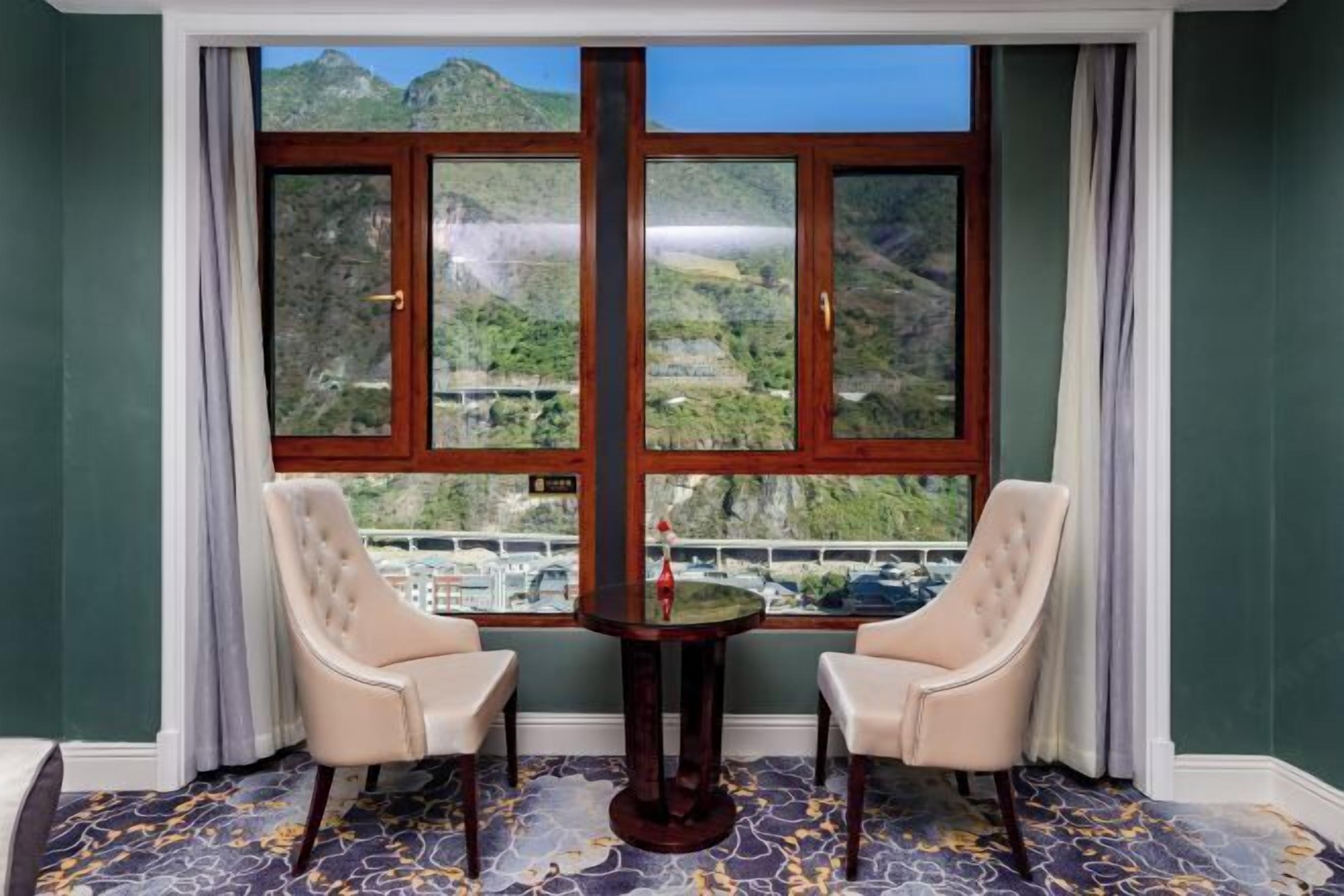 A room with a large window offering a mountain view, two upholstered chairs, and a small table with a decorative item.