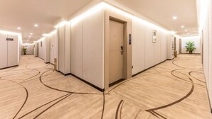 A hotel hallway with a modern design, featuring a carpet with a wavy pattern, recessed lighting, and a series of doors on one side. - Home Inn Yubai Yun Hotel (Zhangjiagang Jingang Central Plaza) (Zhangjiagang)