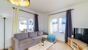 A modern living room with a grey sofa, a coffee table, a TV, and a balcony with curtains.