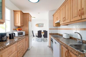 Uma cozinha moderna com armários de madeira, bancadas de granito, um espaço de refeições com mesa e cadeiras, e uma geladeira visível.