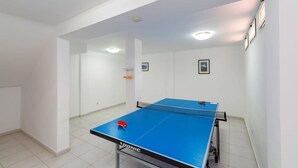 Una mesa de ping pong en una habitación con paredes blancas, suelo de baldosas e iluminación empotrada.