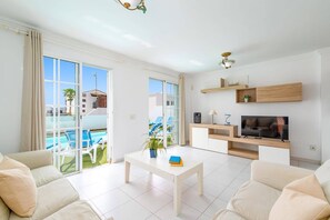 Ein modernes Wohnzimmer mit Fernseher, Sofa und Blick auf einen Pool.