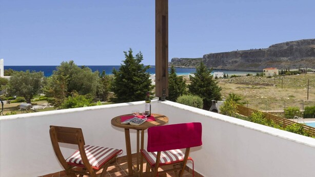 A balcony with two chairs and a table, overlooking a coastal landscape with a clear sky and a view of the sea and cliffs. - Villa Aqua Maris by Villa Plus (Rhodes)