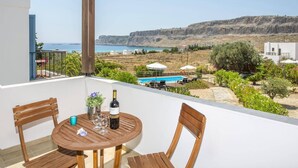 A balcony with a table set for two, overlooking a scenic view of the sea and a mountainous landscape.