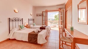 A bedroom with two beds, a wooden desk, a chair, and a balcony with a view. - Villa Badia D'Or by Villa Plus (Cala d'Or)