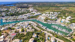 An aerial view of Villa Badaia D'or, featuring a marina with numerous boats, surrounding residential buildings, and a coastal landscape. - Villa Badia D'Or by Villa Plus (Cala d'Or)