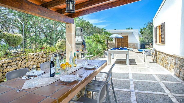 Un patio al aire libre con una mesa de comedor para dos, una mesa de billar y un muro de piedra.