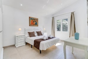 A bedroom with a bed, bedside tables, a window with curtains, and a painting on the wall.