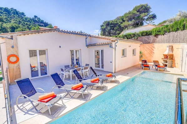 A poolside area with lounge chairs, a dining table, and a small kitchen area.