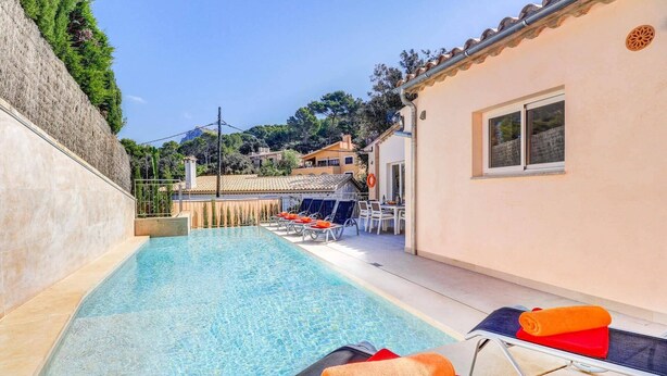 A swimming pool with lounge chairs and a table, surrounded by a building with a tiled roof and a view of the hills. - Villa Zaragoza by Villa Plus (Cala Sant Vicenç)