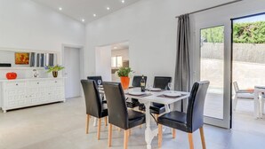 A modern dining area with a white table, black chairs, and a view through a glass door. - Villa Zaragoza by Villa Plus (Cala Sant Vicenç)