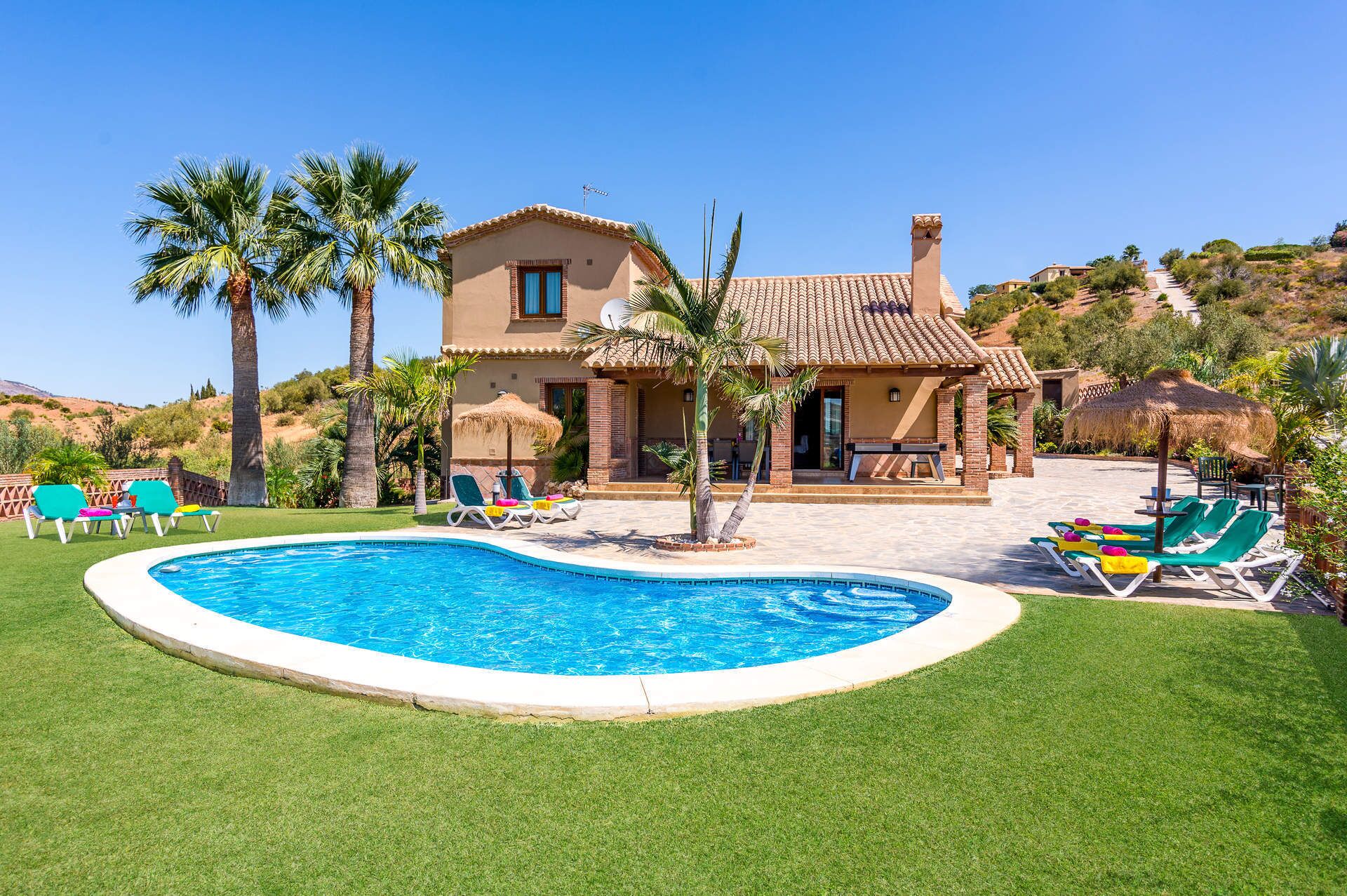Ein zweistöckiges Haus mit Swimmingpool, umgeben von Palmen und einem gepflegten Rasen.