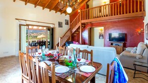 Un espace repas avec une table en bois mise pour le repas, un escalier menant à un niveau supérieur et un coin salon avec un canapé et une télévision.