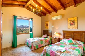 A room with two beds, a window with a view, a chandelier, and a wall-mounted air conditioner.