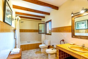 A bathroom with a bathtub, two toilets, a sink, and a mirror.