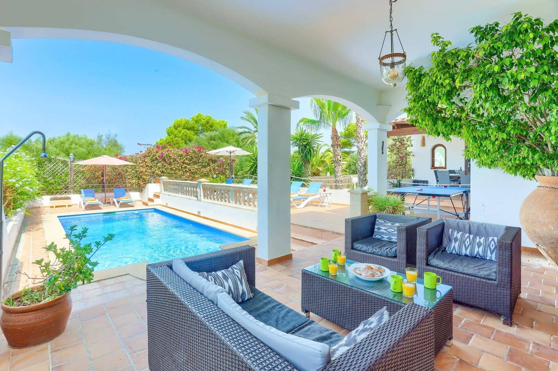 Un espace extérieur avec une piscine, des meubles en osier, une table où sont disposés des aliments pour le petit-déjeuner et une vue sur la piscine.