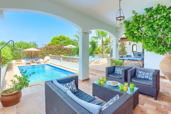 An outdoor pool area with wicker furniture, a table with breakfast items, and a view of the pool.