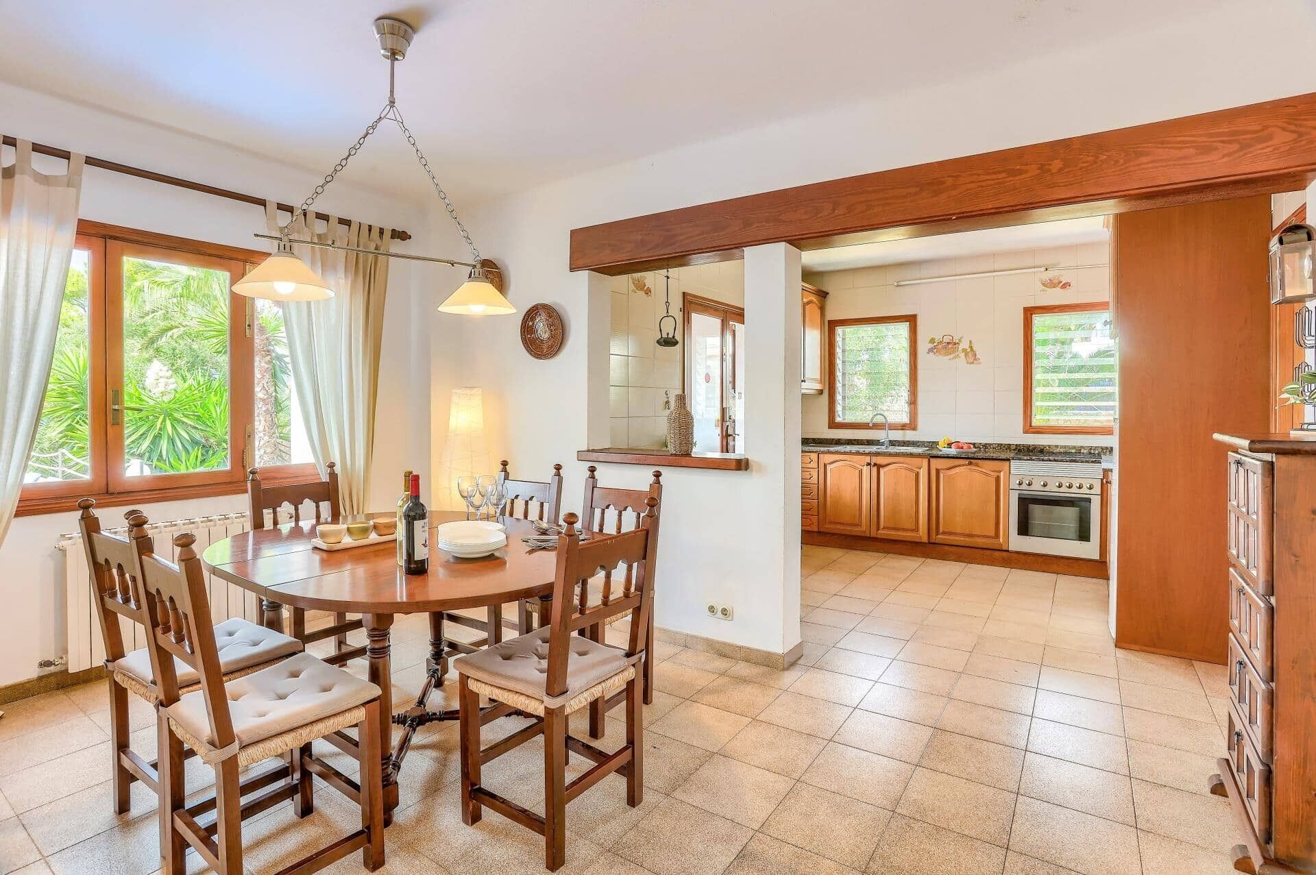 Un comedor con mesa y sillas de madera, una araña y vistas a la cocina con armarios y estufa de madera.