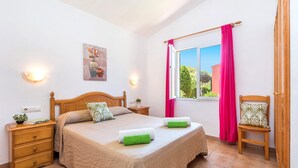 Una camera da letto con un letto, comodini, una sedia, una finestra con tende e un quadro appeso al muro.
