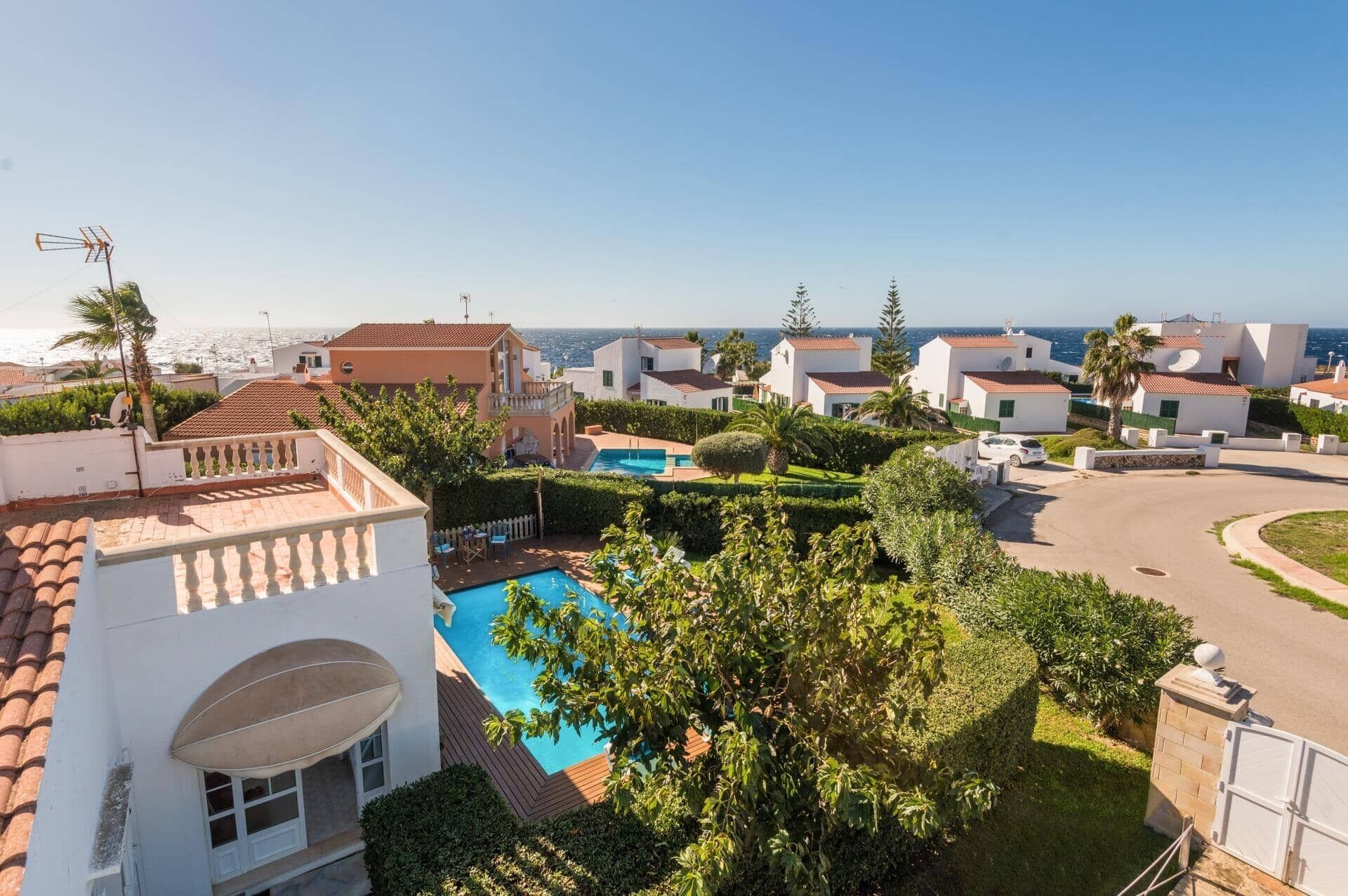 A residential area with a swimming pool, white houses, and a view of the sea.