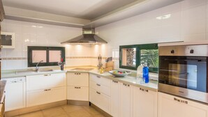 Een moderne keuken met witte kasten, een ingebouwde oven en een raam met uitzicht op groen.