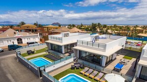 A modern hotel with two swimming pools, outdoor seating, and a view of the beach. - Villa Alana by Villa Plus (Corralejo)