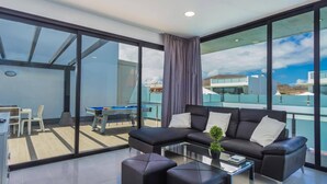 A modern living room with a sectional sofa, a glass coffee table, and a view of the cityscape through large windows. - Villa Alana by Villa Plus (Corralejo)