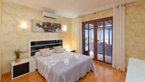Una camera da letto con un letto, comodini, condizionatore d'aria a muro, una porta scorrevole in vetro su un balcone e una plafoniera.