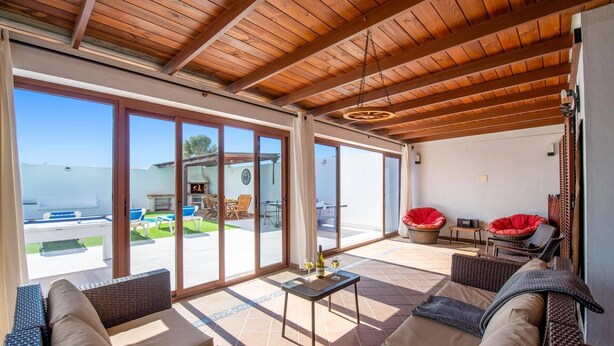 Un'ampia veranda con tetto in legno, grandi porte scorrevoli in vetro e mobili in vimini, con vista sull'esterno.