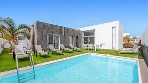 A modern poolside area with a clear blue pool, lounge chairs, and a dining table. - Villa Yucca Mar by Villa Plus (Playa Blanca)