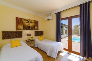 Ett hotellrum med två sängar, en stor målning av Buddha, en luftkonditionering och utsikt över en swimmingpool.