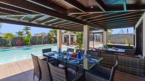 An outdoor pool area with a covered seating area, a dining table set for two, and a statue in the background. - Villa Zen by Villa Plus (Montaña Roja)