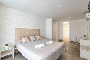 A modern bedroom with a large bed, a bedside table, a small plant, and a bathroom visible through an open door.