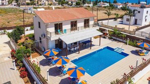A two-story building with a rooftop terrace, a swimming pool, and outdoor seating with umbrellas.