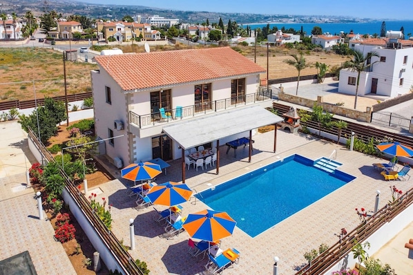 A two-story building with a rooftop terrace, a swimming pool, and outdoor seating with umbrellas.