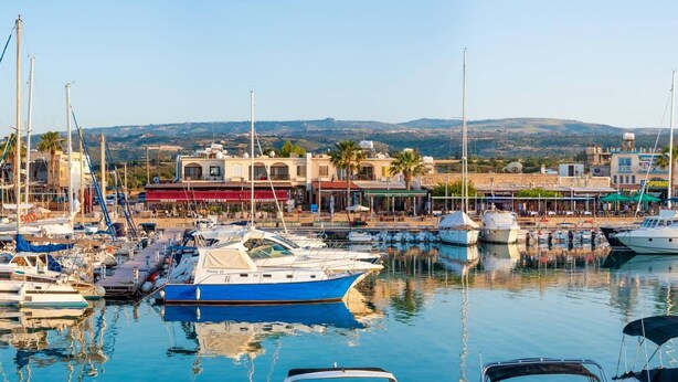 A marina with boats docked, a building with a restaurant, and a view of hills in the background.