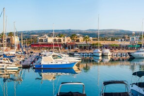 Un puerto deportivo con barcos amarrados, un edificio con restaurante y vistas a colinas al fondo.