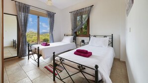 A bedroom with two beds, a window with curtains, a hanging light fixture, and a view of greenery outside. - Villa Andriana by Villa Plus (Latchi)