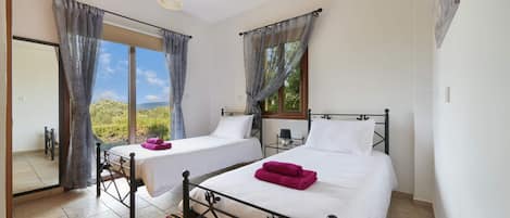 Un dormitorio con dos camas, una ventana con cortinas, una lámpara colgante y vistas al exterior con vegetación.