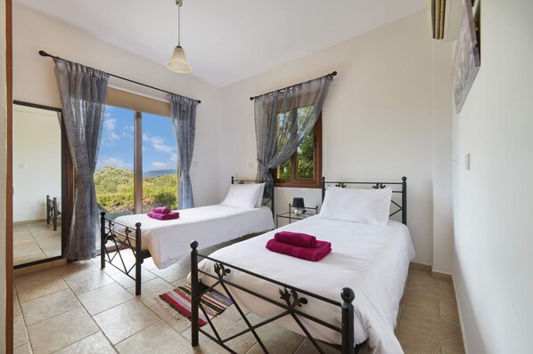 Un dormitorio con dos camas, una ventana con cortinas, una lámpara colgante y vistas al exterior con vegetación.