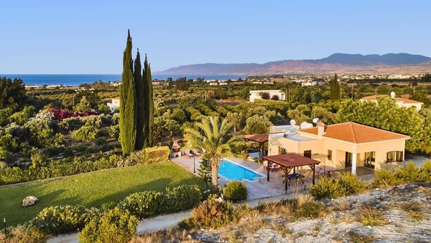A Mediterranean-style villa with a swimming pool, surrounded by lush gardens and cypress trees, overlooking a coastal town and mountains. - Villa Andriana by Villa Plus (Latchi)