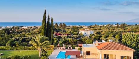 A residential area with a swimming pool, a house with a red roof, and a view of the sea.
