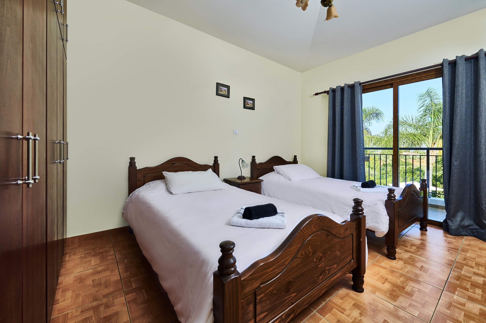 A bedroom with two wooden beds, a wardrobe, and a balcony with curtains.